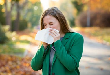 Woman standing outside sneezing into a tissue