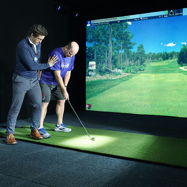 Provider working with a patient using a golf simulator.