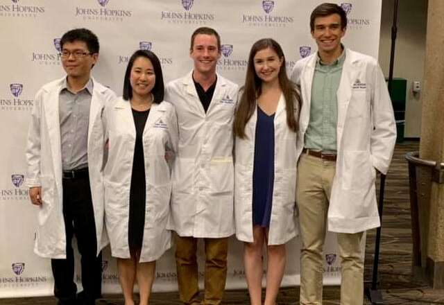 A group of graduate students pose together in their new white coats.