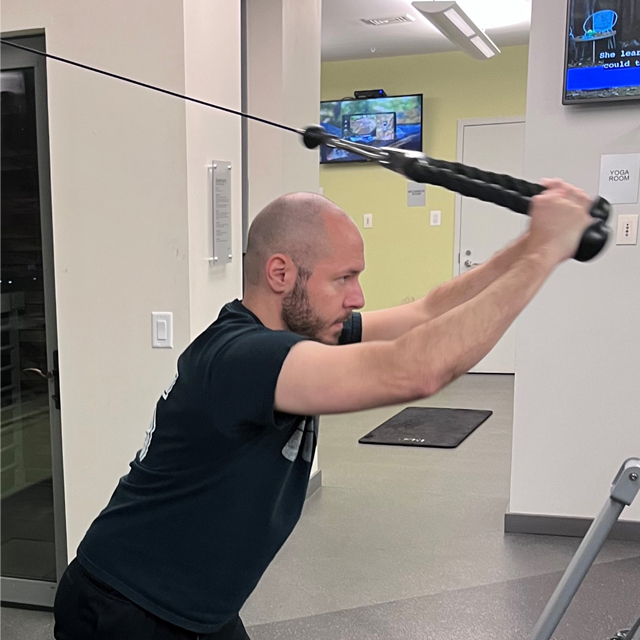 James is shown at the gym, wearing a dark t-shirt and using a weight machine