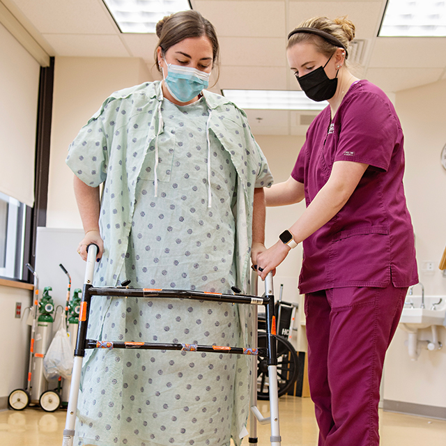 A patient walks with the aid of a nurse and a walker.