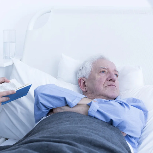 An elderly man lays in his hospital bed pouting
