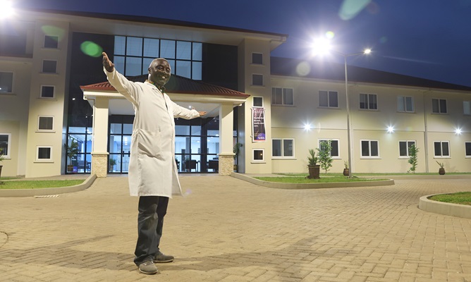 Boahene stands, arms out, in-front of the newly opened hospital.