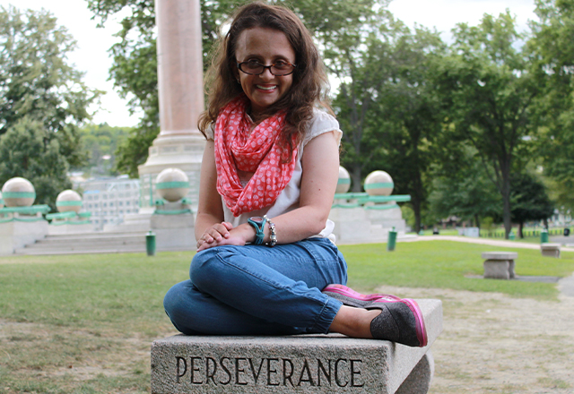 Lauren Loose sits on a stone pedestal that reads, "Perseverance ."