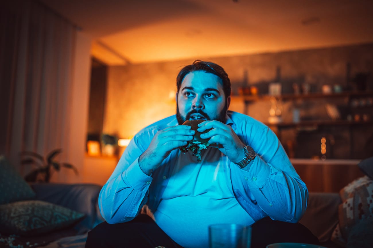 Guy watching TV and eating a hamburger