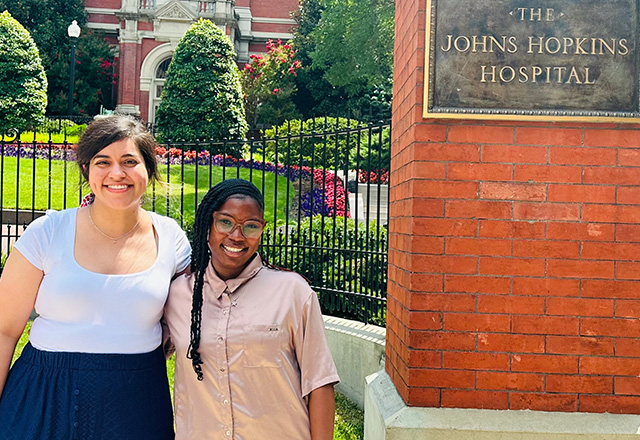 Melody Rorabeck and Kenara Ford standing in front of the gated entrance of The Johns Hopkins Hospital