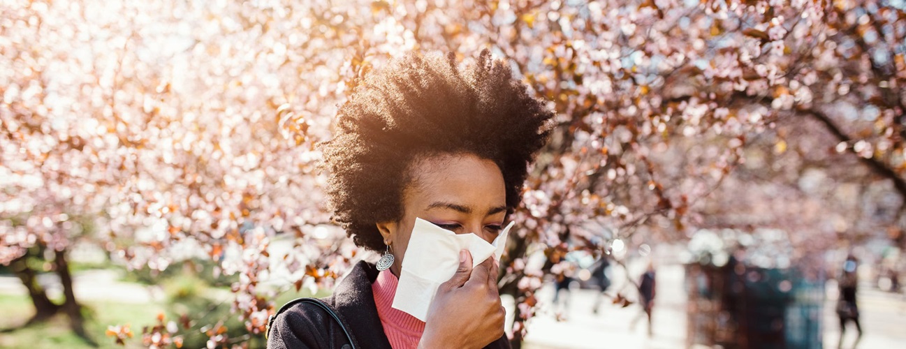 Woman with seasonal allergies sneezing near blossoming trees