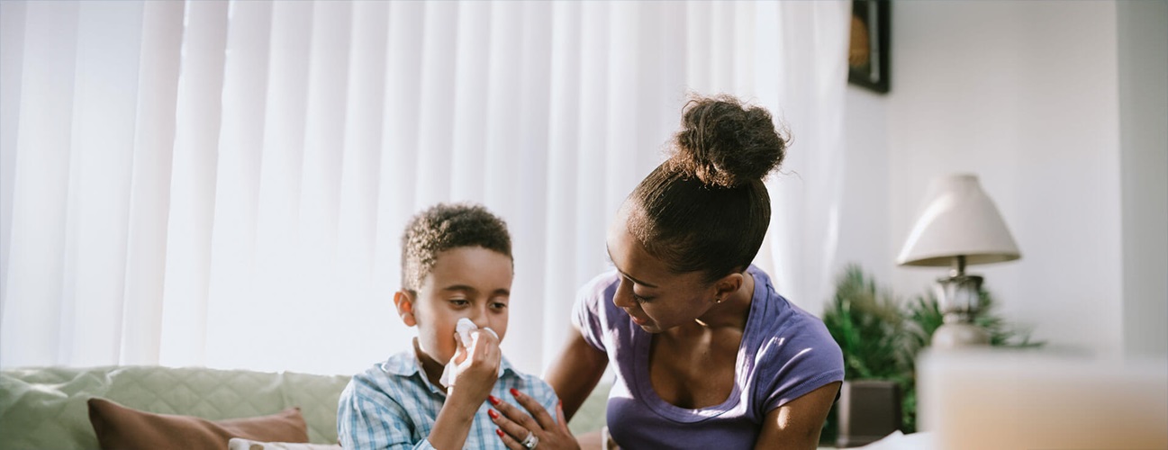 A mother helps her son blow her nose as he suffers from pertussis in children
