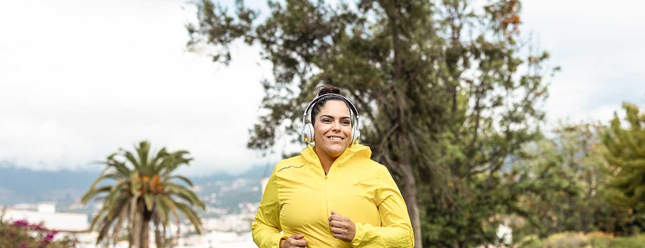 Woman jogging through lush park in a bright yellow jacket