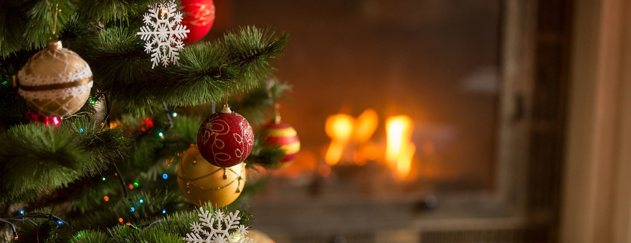 Decorated holiday tree inside of a home with a warm fireplace in the background
