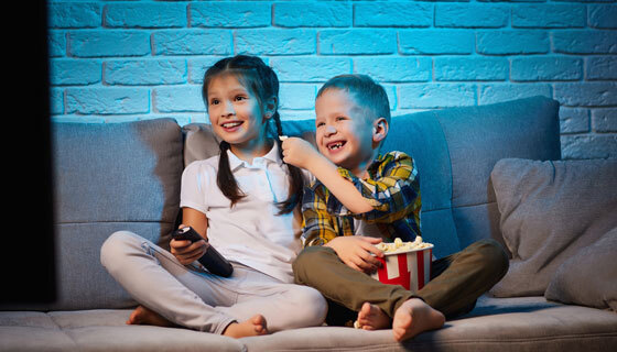 two children sit on the couch watching television
