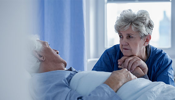 woman holding a man's hand who is laying in bed