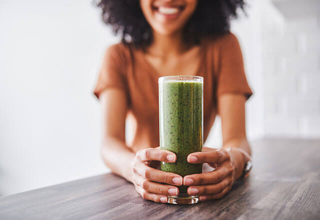 a woman holds a glass containing a healthy green smoothie