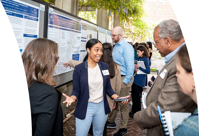 Young woman standing in front of a poster conversing with Dr. Otis Brawley and others.