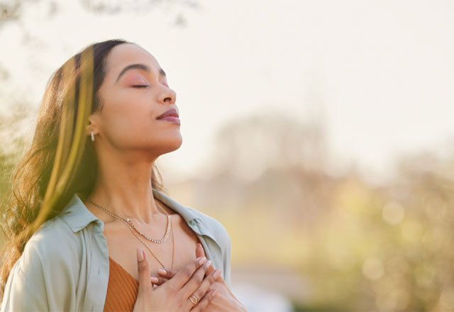A woman standing outside practicing a breathing meditation.