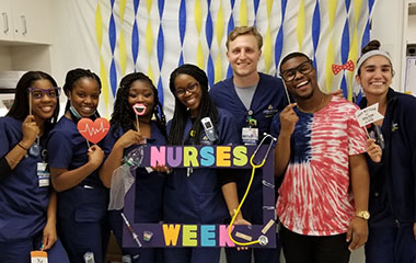 Seven smiling nurses pose together in pre-COVID times. 